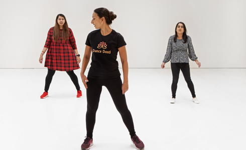 Three global majority female dancers. one standing front and centre with two further back each side. All wearing casual clothes on a white background 