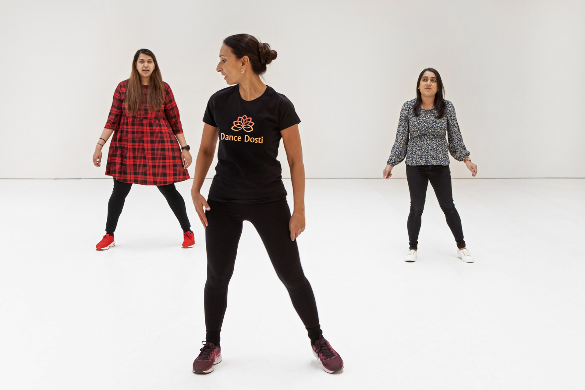 Three global majority female dancers. one standing front and centre with two further back each side. All wearing casual clothes on a white background 