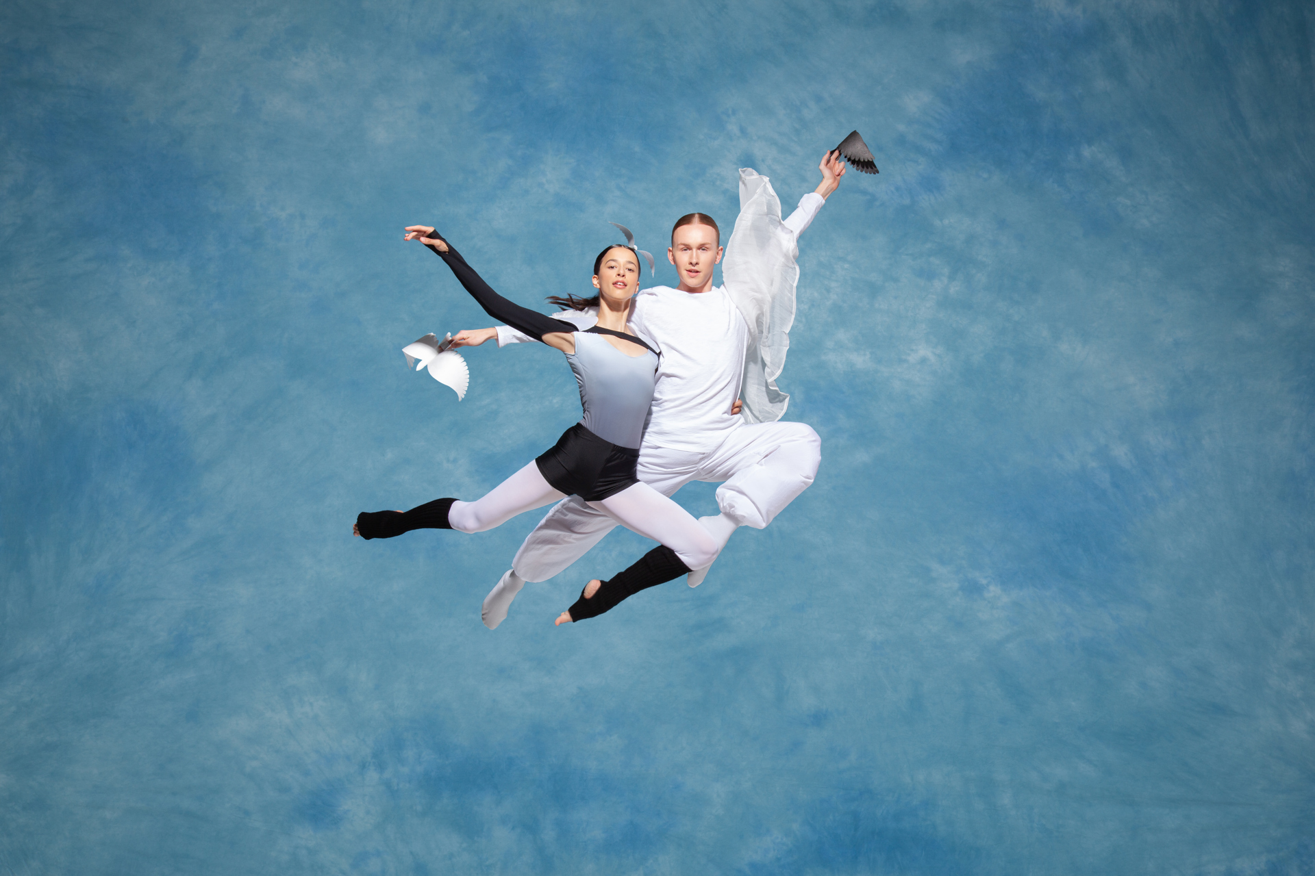 Two ballet dancers jumping in the air with a cloudy blue background