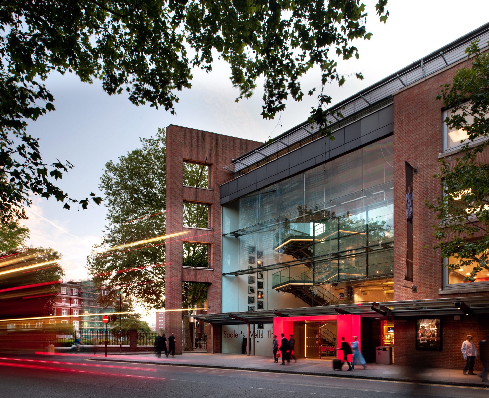 Image of the new Sadlers Wells Theatre. Large brick building with large windows with lit up red door