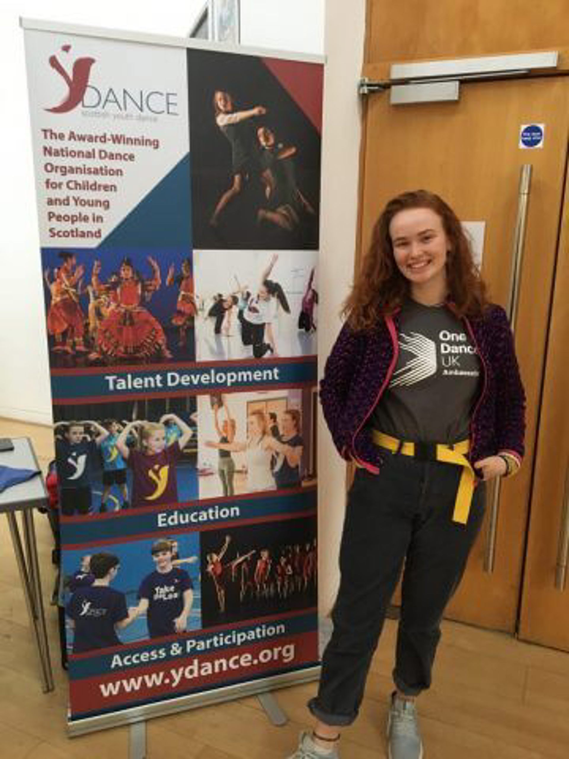 White female one dance uk dance ambassador standing in front of a Y Dance pull up banner