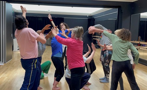 group of adults in colourful clothes in a dance studio moving around each other 