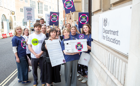 fourteen adults mixed genders standing in a group holding signs that say save our subjects outside the department of education