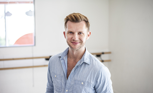 Headshot of Cameron Ball. White blonde male smiling at the camera wearing blue button up shirt 