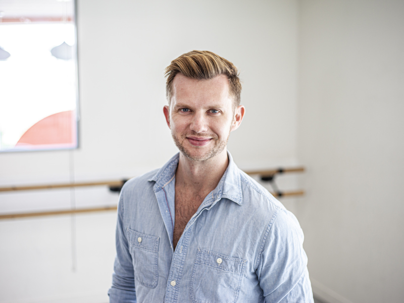 Headshot of Cameron Ball. White blonde male smiling at the camera wearing blue button up shirt 