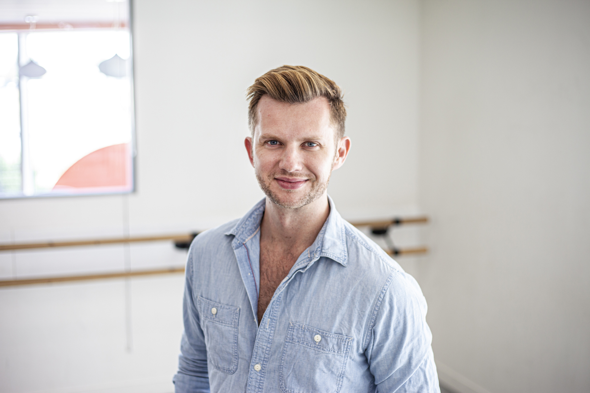 Headshot of Cameron Ball. White blonde male smiling at the camera wearing blue button up shirt 