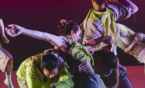 six dancers moving together in front of a striped pick and purple background