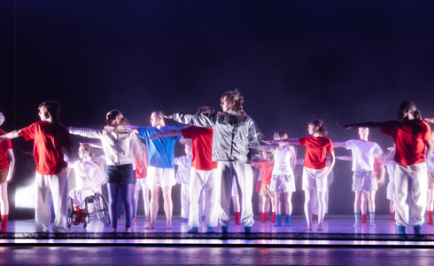 youth group on purple stage all wearing bright white, red and blue colourful casual clothes all pointing to the left. 