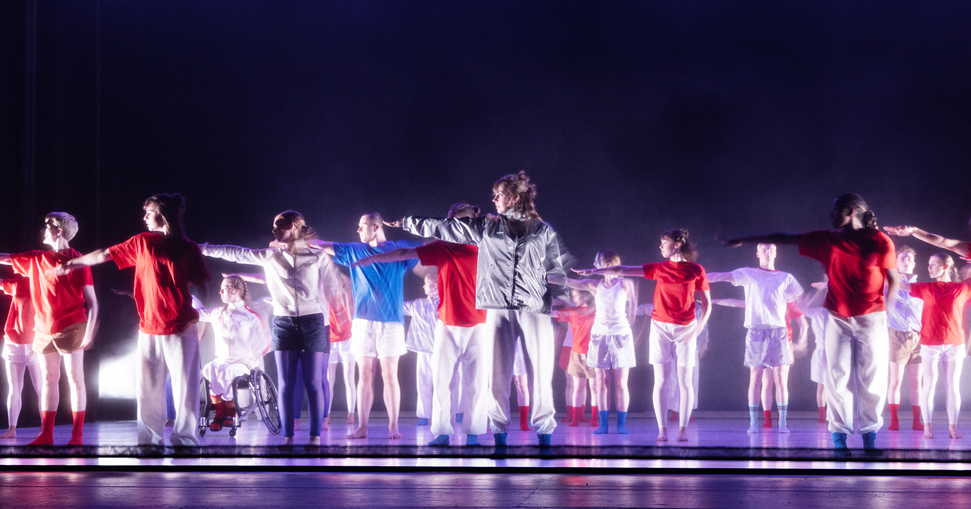 youth group on purple stage all wearing bright white, red and blue colourful casual clothes all pointing to the left. 