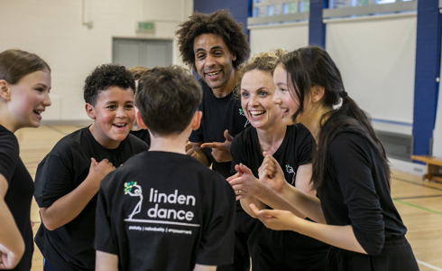 teachers and dance students excitedly talking together in black PE kit with sports hall