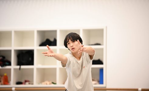 global majority male dancer in a white studio reaching forward 