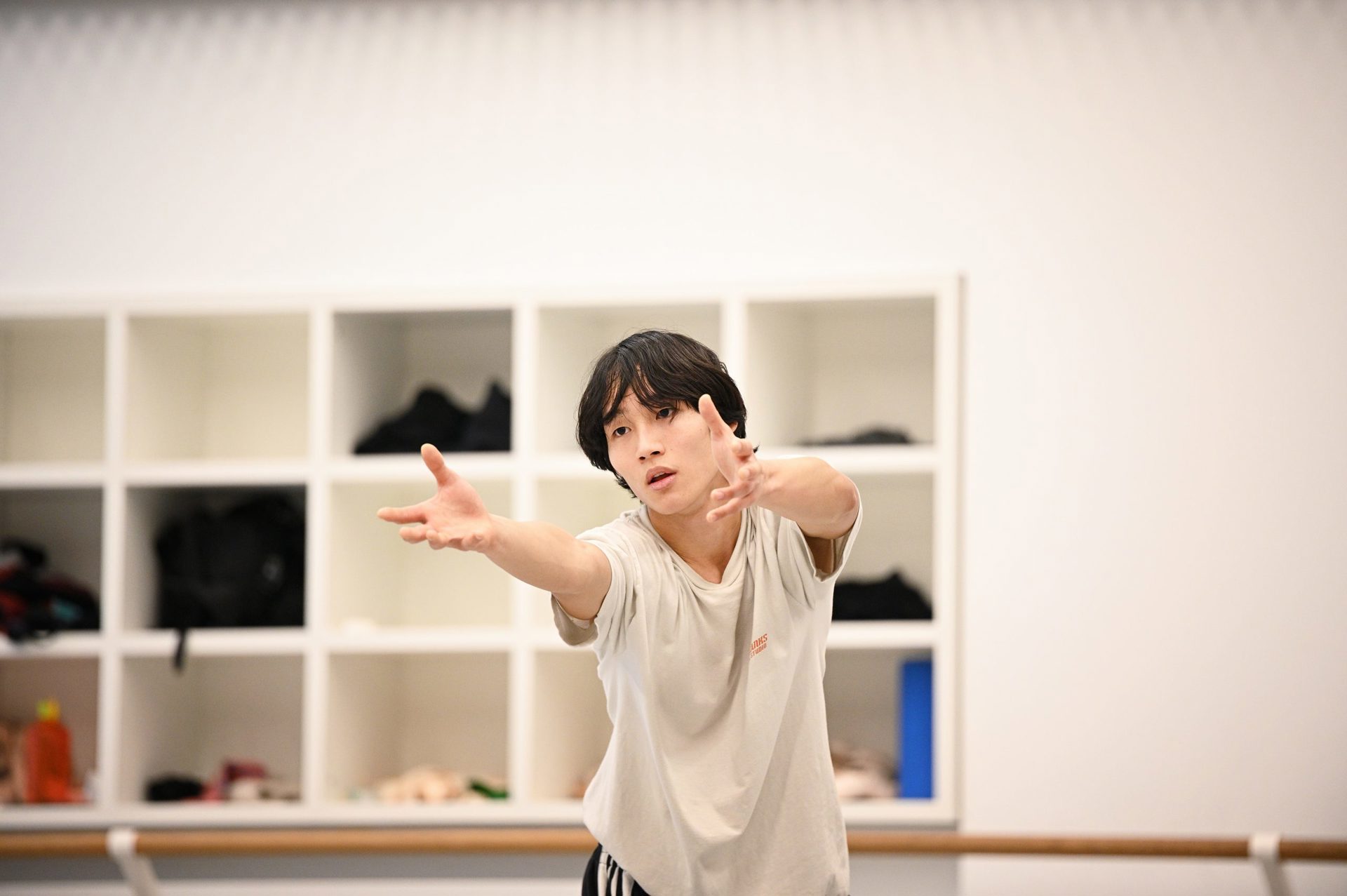 global majority male dancer in a white studio reaching forward 