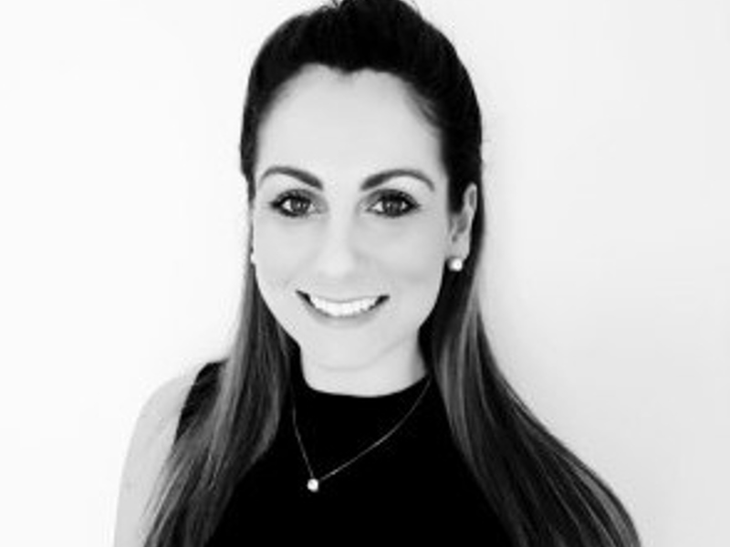 Black and white headshot of Louise Kelsey. White female with long hair smiling at the camera