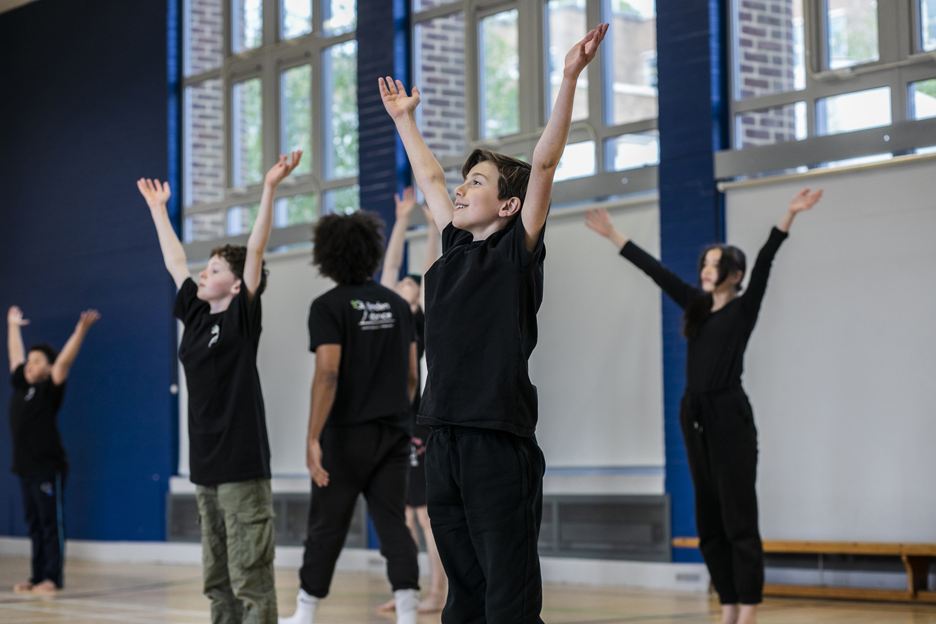 primary school boys and girls all reaching up to the sky in a sports hall