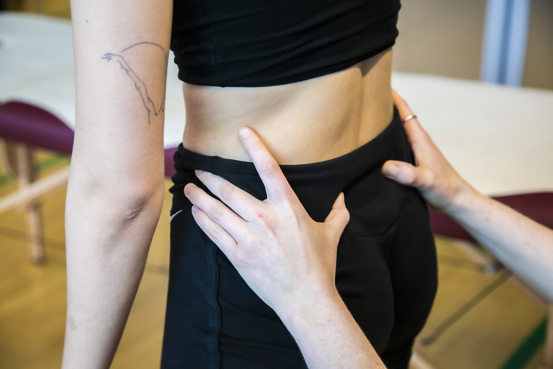 Close up of healthcare practitioners hands on the small of dancers back asthey stand. 