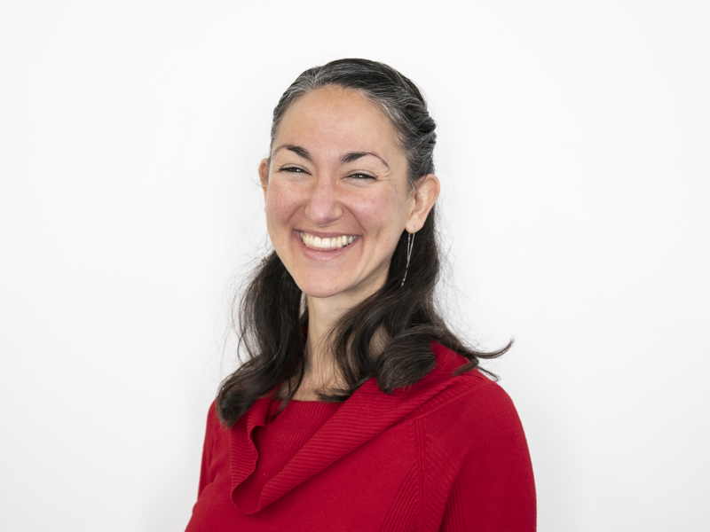 Headshot of Erin Sanchez. female with short brown smiling at the camera wearing red jumper with white background