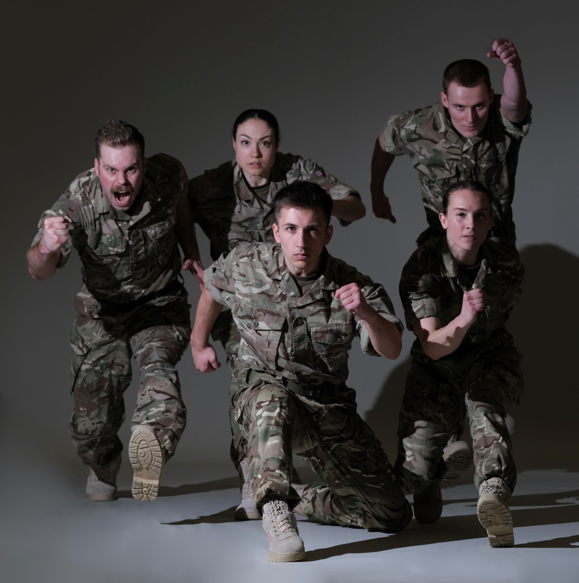 five dancers dressed as soldiers running towards he camera on a grey background 