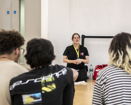 One Dance UK staff member sitting on knees talking to three students sitting in front of the camera in a dance studio. 