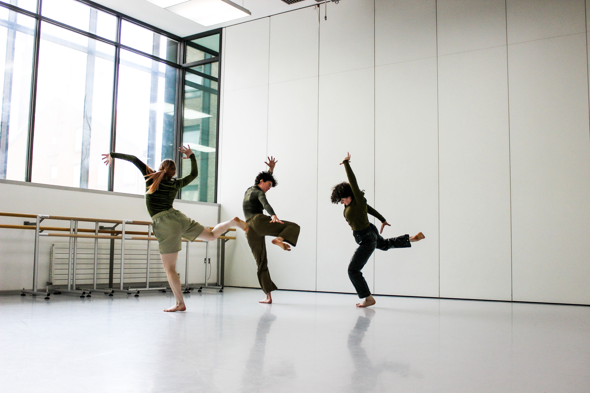 three people dancing in a dance studio with large white walls and large windows 